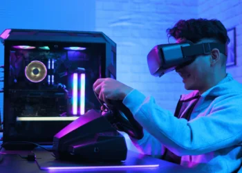 Os 10 Melhores Volantes Gamer de 2024: Logitech, Thrustmaster e mais! 2 ovem gamer sorridente usando um dos Melhores Volantes Gamer de 2024 com um PC de alta performance e iluminação RGB.