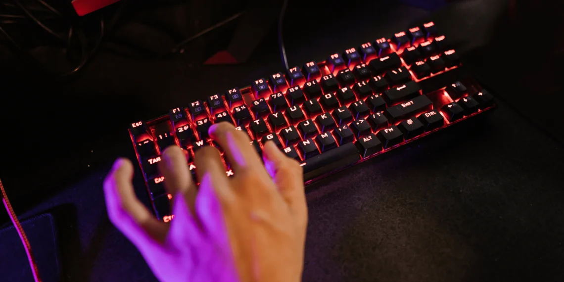Mão de um jogador usando um teclado gamer com iluminação RGB vermelha.