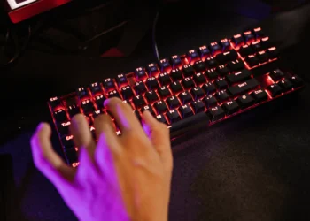 Mão de um jogador usando um teclado gamer com iluminação RGB vermelha.