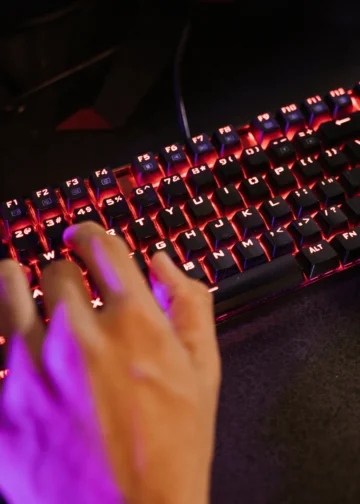 Mão de um jogador usando um teclado gamer com iluminação RGB vermelha.