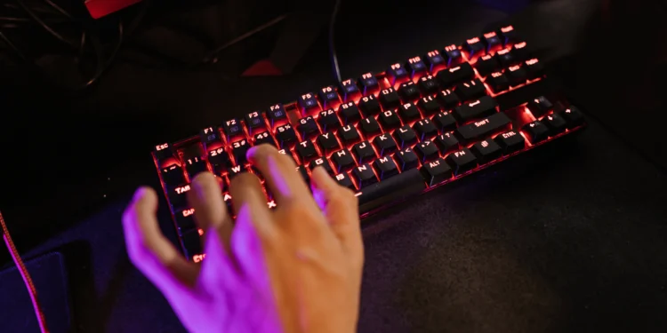 Mão de um jogador usando um teclado gamer com iluminação RGB vermelha.