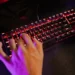 Melhor teclado gamer: Os 10 melhores em 2024! 33 Mão de um jogador usando um teclado gamer com iluminação RGB vermelha.