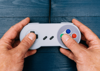 Os 10 Melhores Videogames Antigos para Comprar em 2024 7 Mãos segurando um controle de um dos melhores videogames antigos.