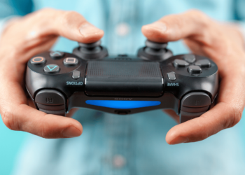 Como Jogar Com controle de PS4 no PC, Veja agora! 11 Mãos segurando um controle de PS4, com um fundo azul claro, pronto para jogar no PC.