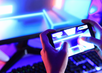20 Melhores Jogos para Android em 2024 27 Jogador interagindo com um jogo no celular enquanto o PC está ao fundo, representando a evolução dos jogos mobile em 2024.